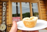 a person holding up a butter tart on a plate in front of a coffee sign